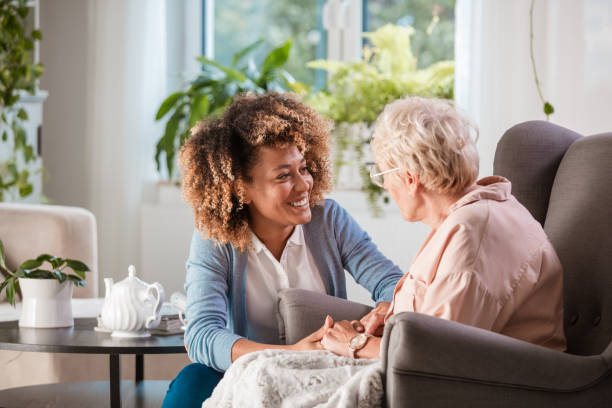 Female home caregiver talking with senior woman, sitting in living room and listening to her carefully.